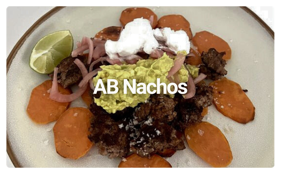 A plate of nachos with beef, sliced carrots, guacamole, sour cream, jalapenos, and a lime wedge, labeled 'AB Nachos'.
