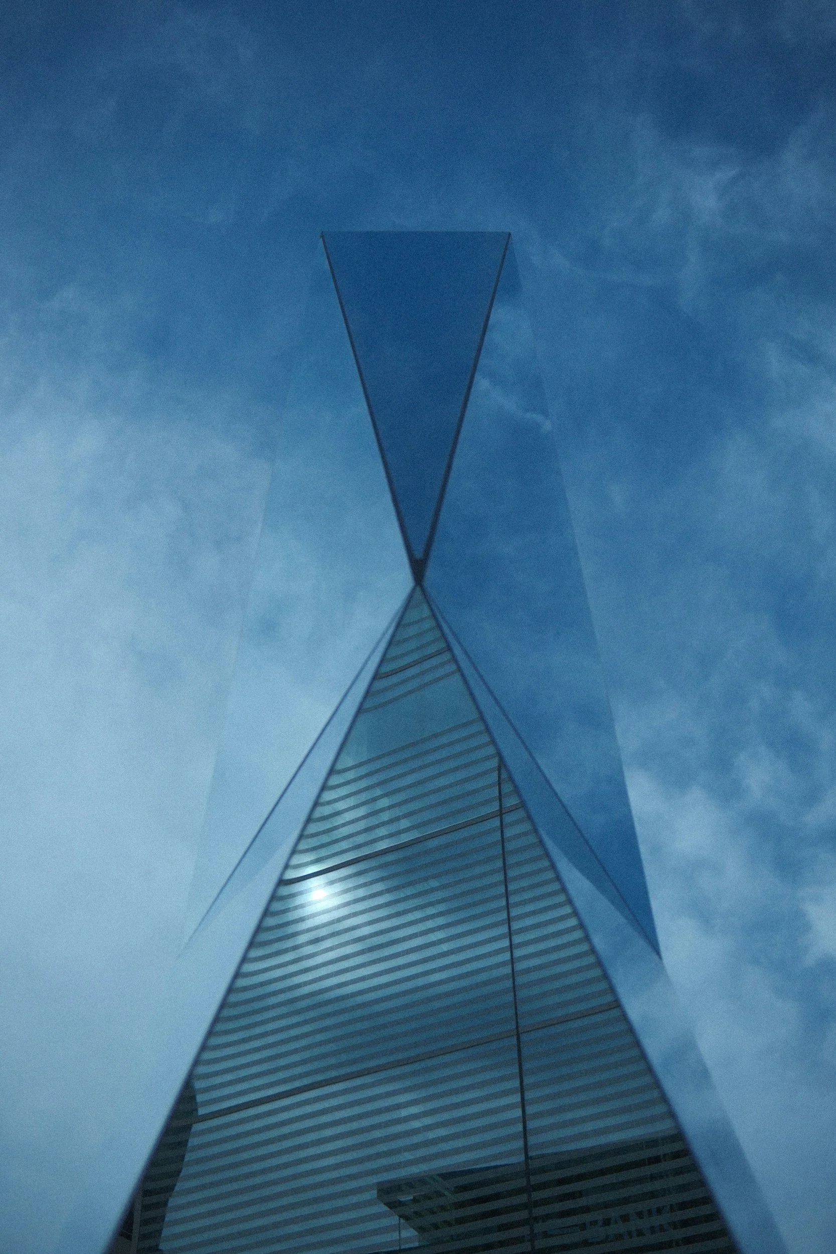 A tall modern glass skyscraper viewed from below against a blue sky with clouds.
