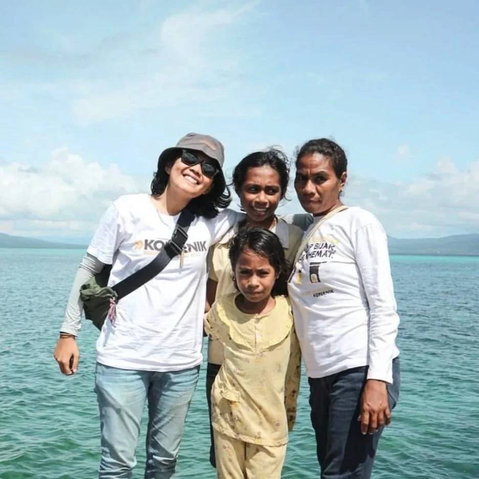 Four women and a girl standing together on a boat or pier with a body of water and mountains in the background, smiling and posing for the photo.