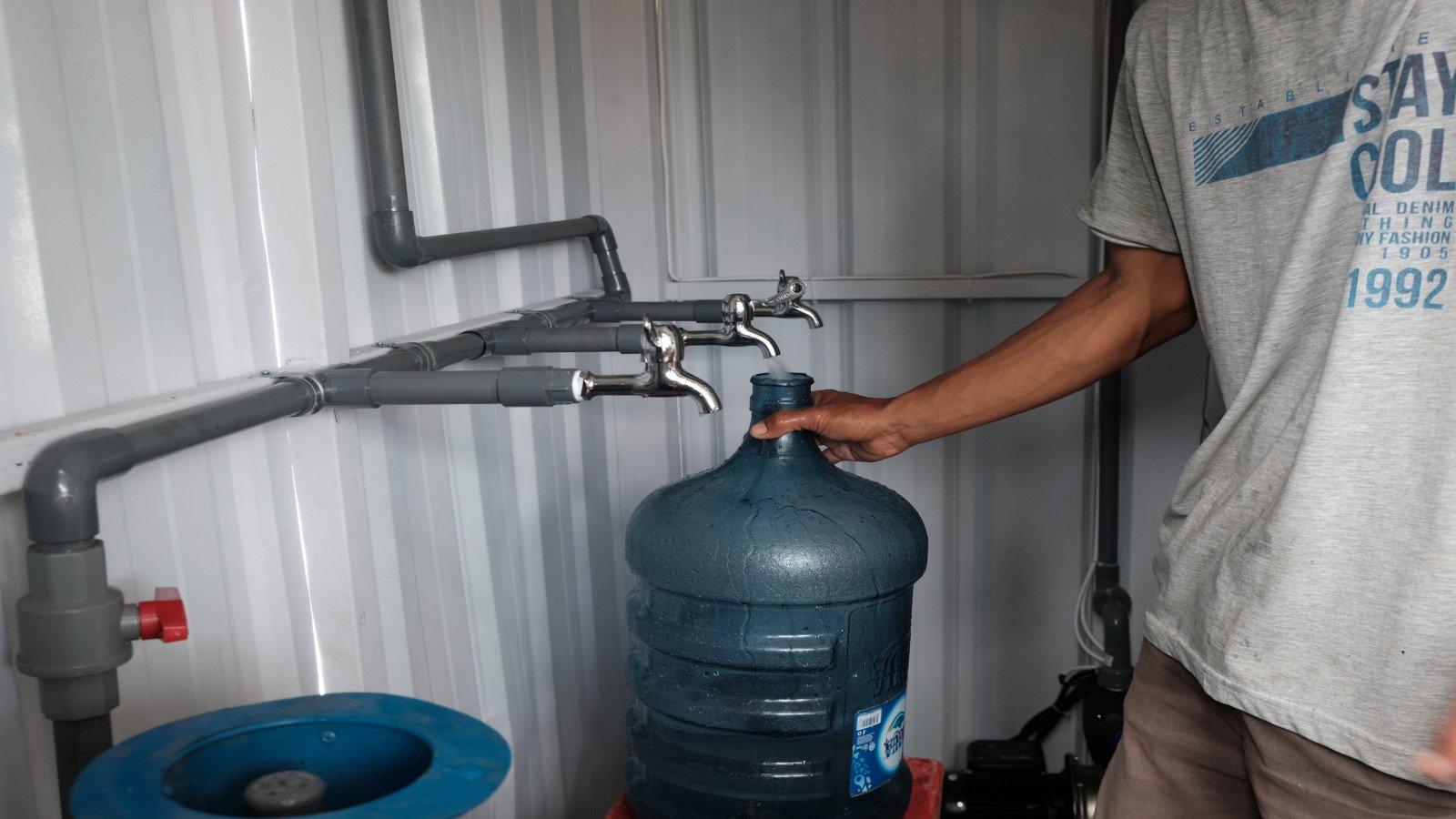 Person filling a large water jug from a faucet at an indoor water station.
