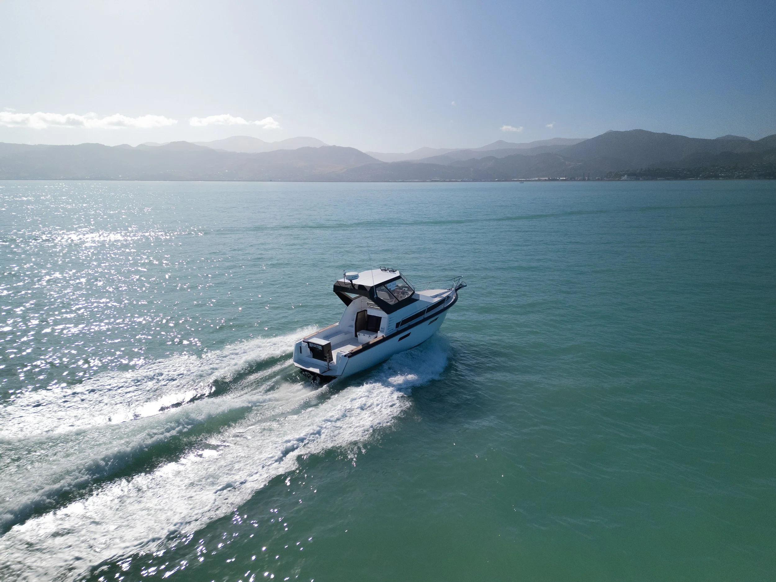 A white motorboat speeding across a large body of water with mountains in the background under a clear blue sky.