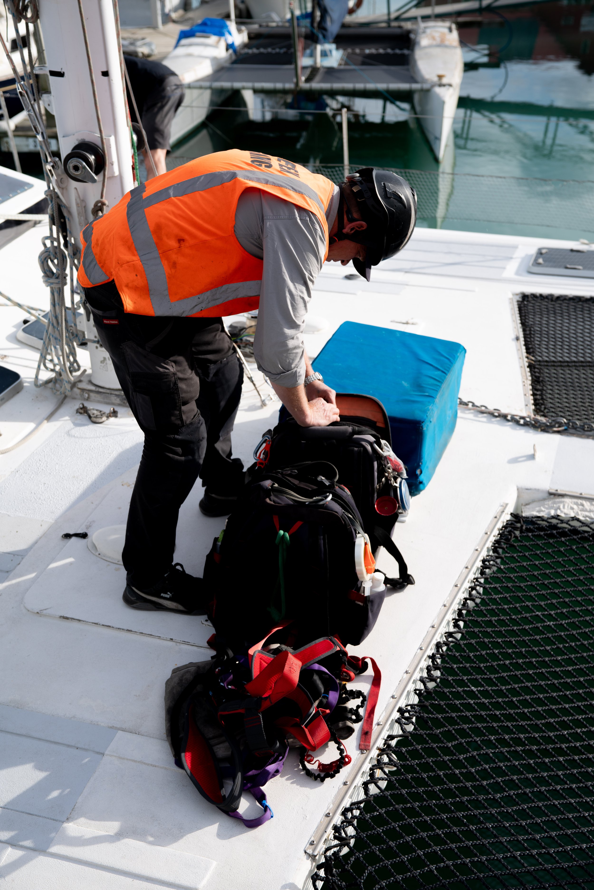 A person wearing a safety vest and helmet on a boat, organizing bags and gear on the deck.