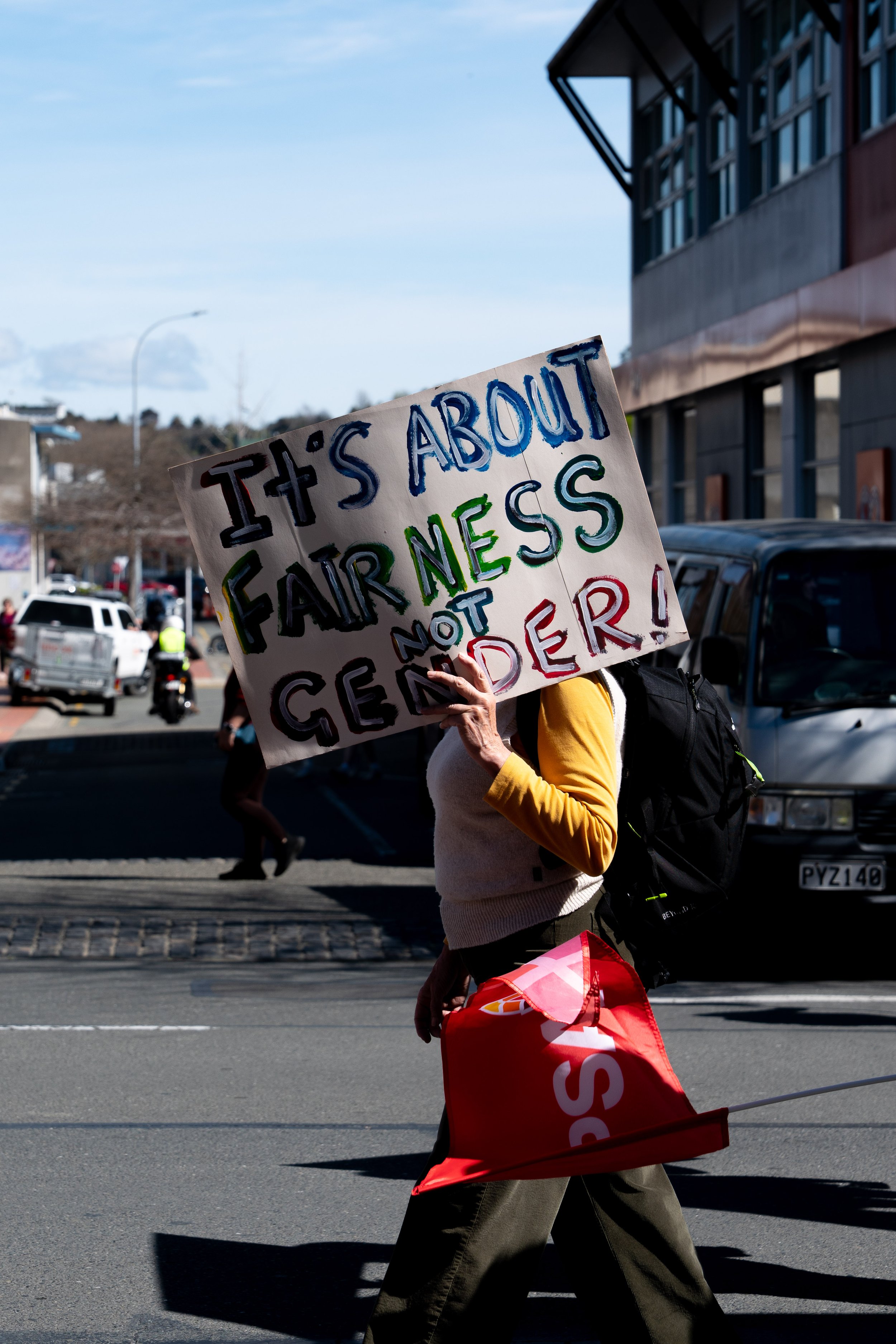 Person holding a sign that reads 'It's about fairness, not cender!,' walking in a street protest or demonstration.