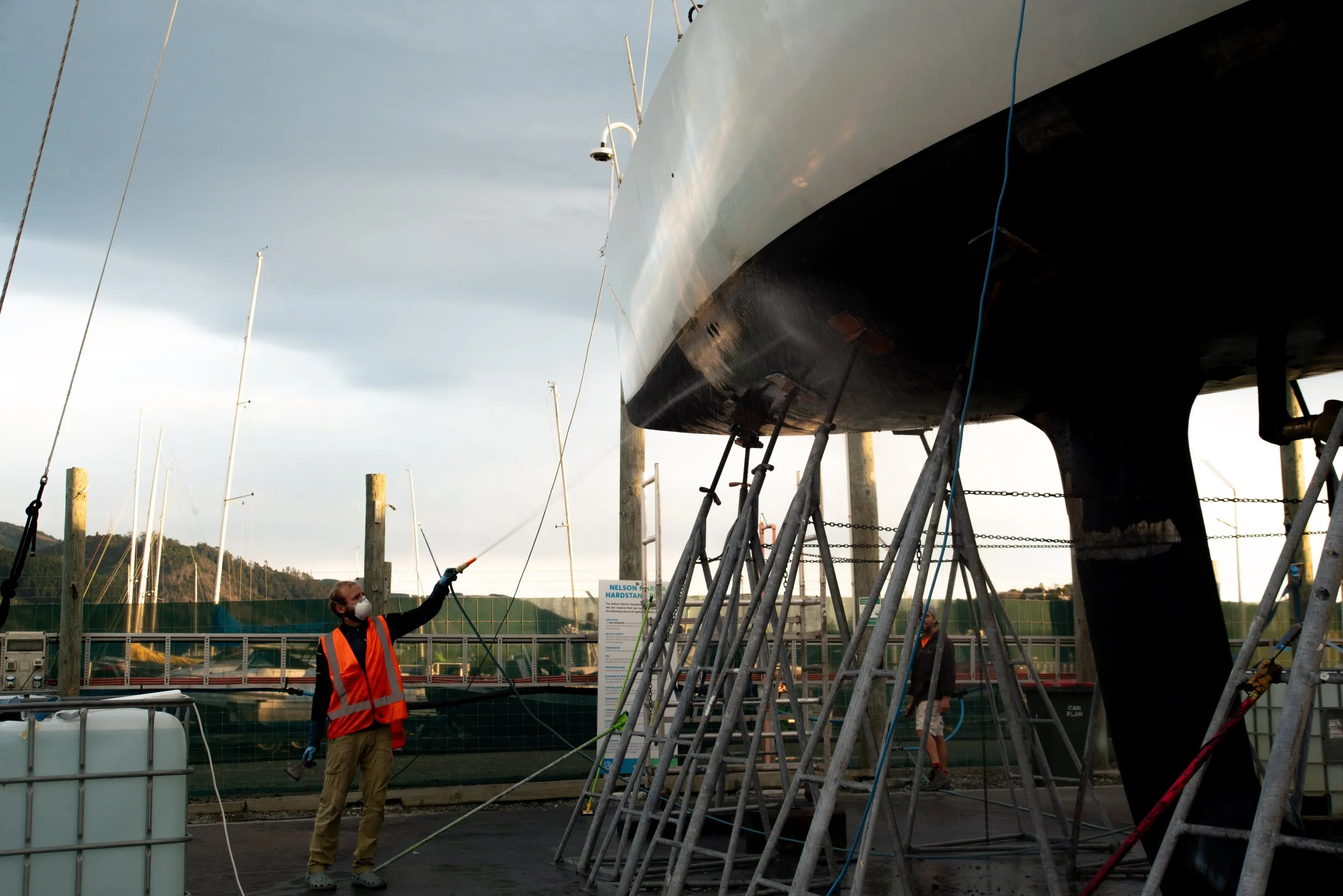 Workers cleaning the hull of a sailboat that is on a boat lift at a marina.