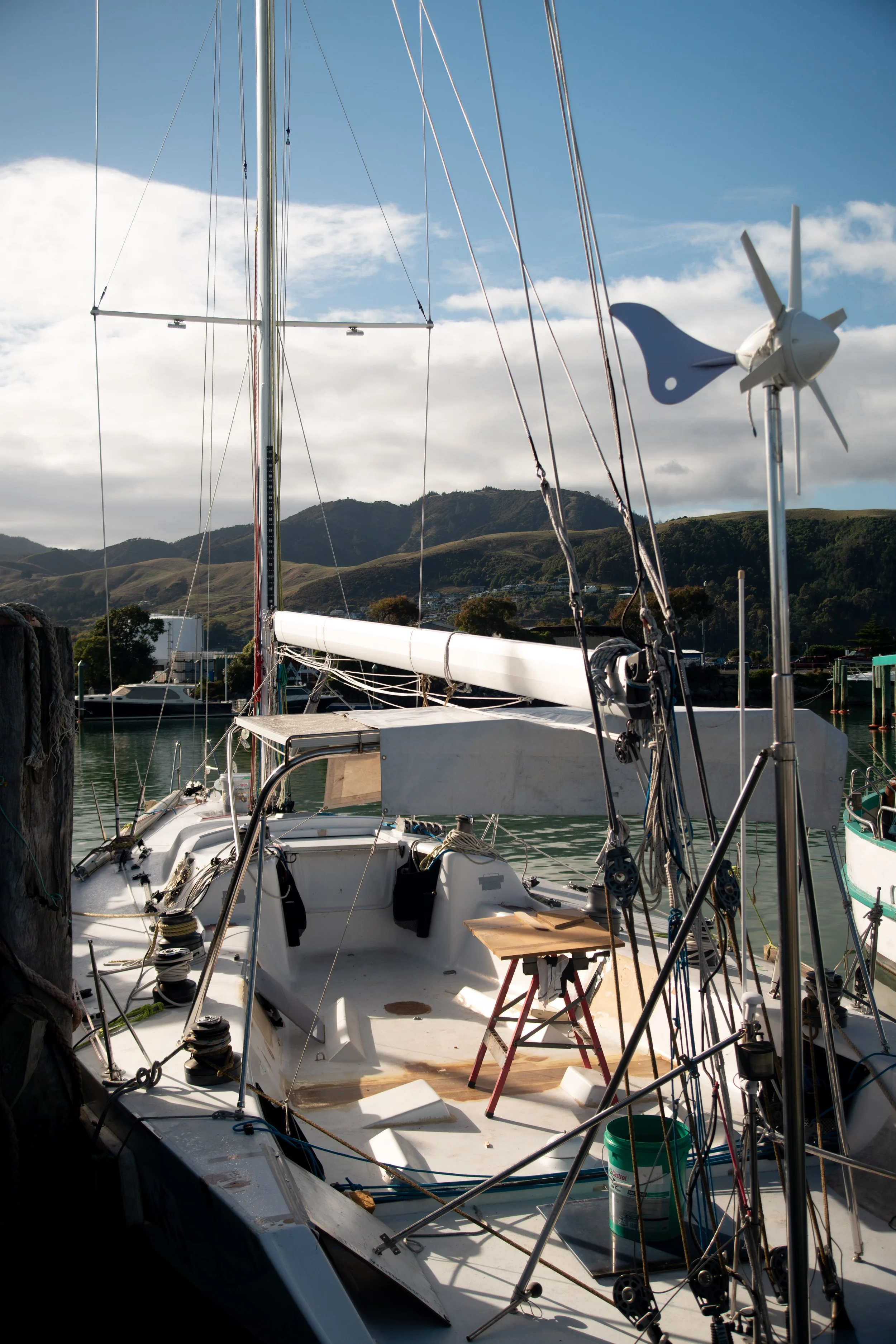 View of a sailboat docked at a marina with hills and a partly cloudy sky in the background.