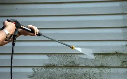 Person pressure washing a dirty horizontal metal surface.