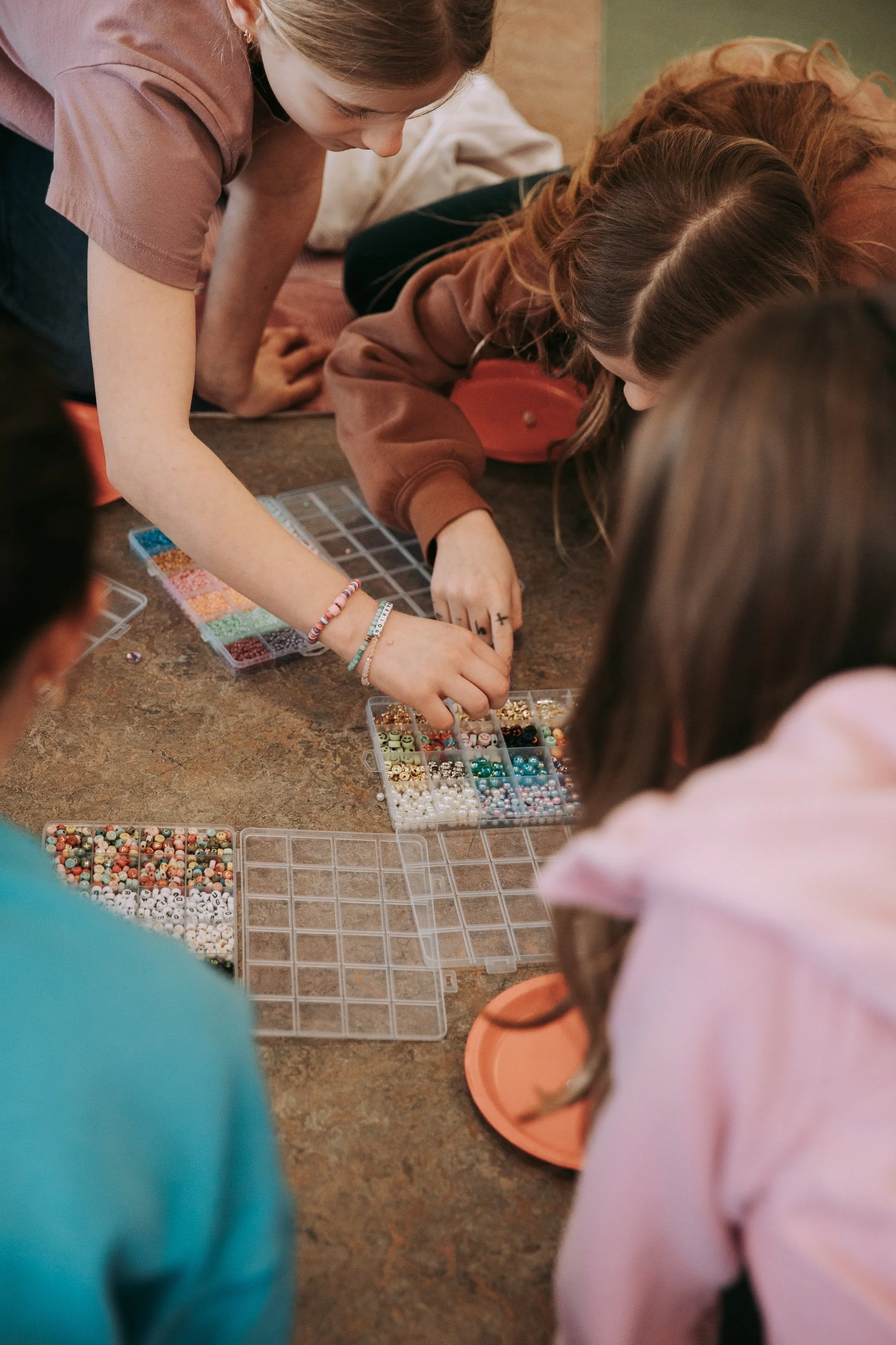 Children gathered around organizing colorful beads in plastic containers on a table.