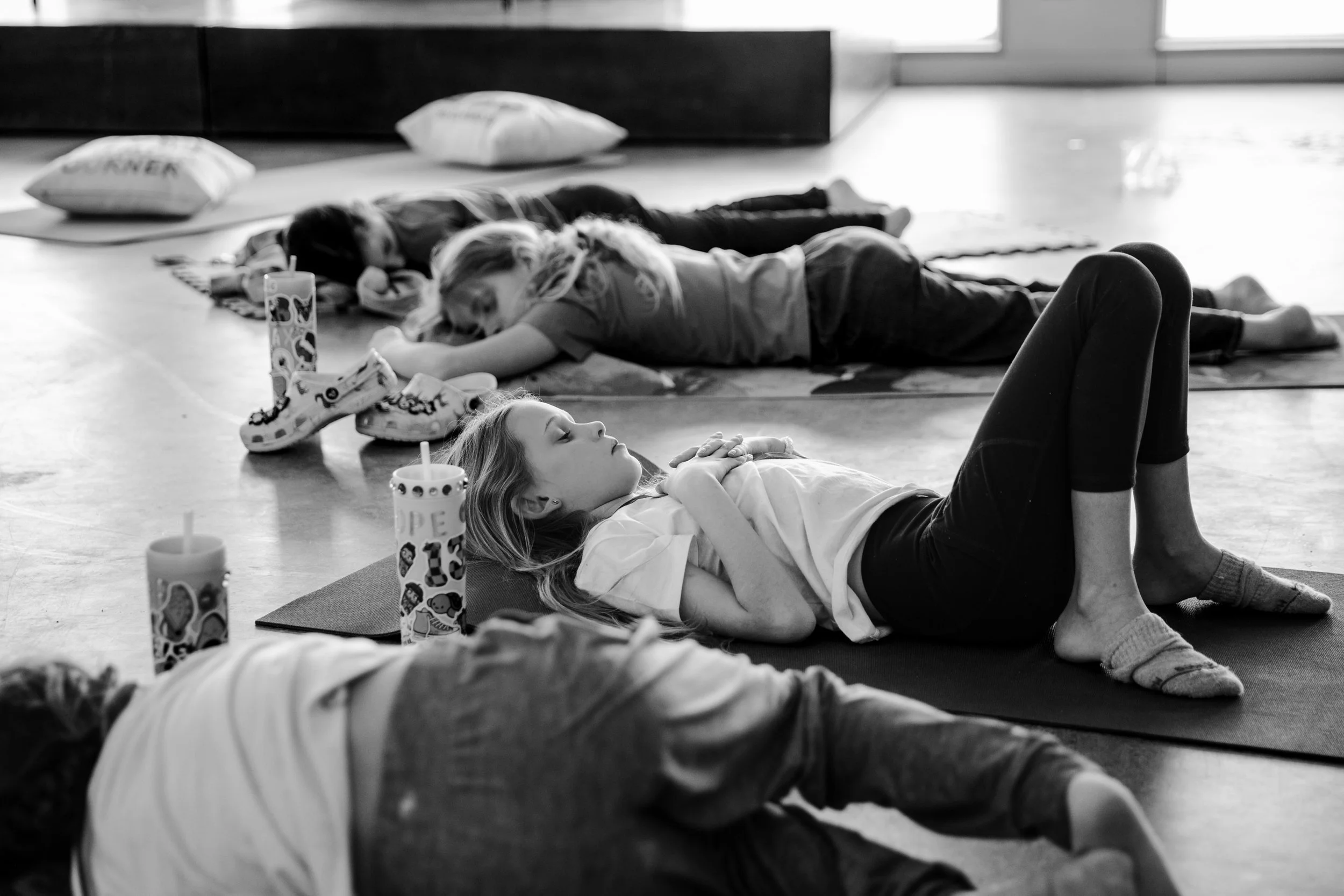 Children lying on yoga mats, resting or sleeping during a group activity or class in a bright room with large windows.