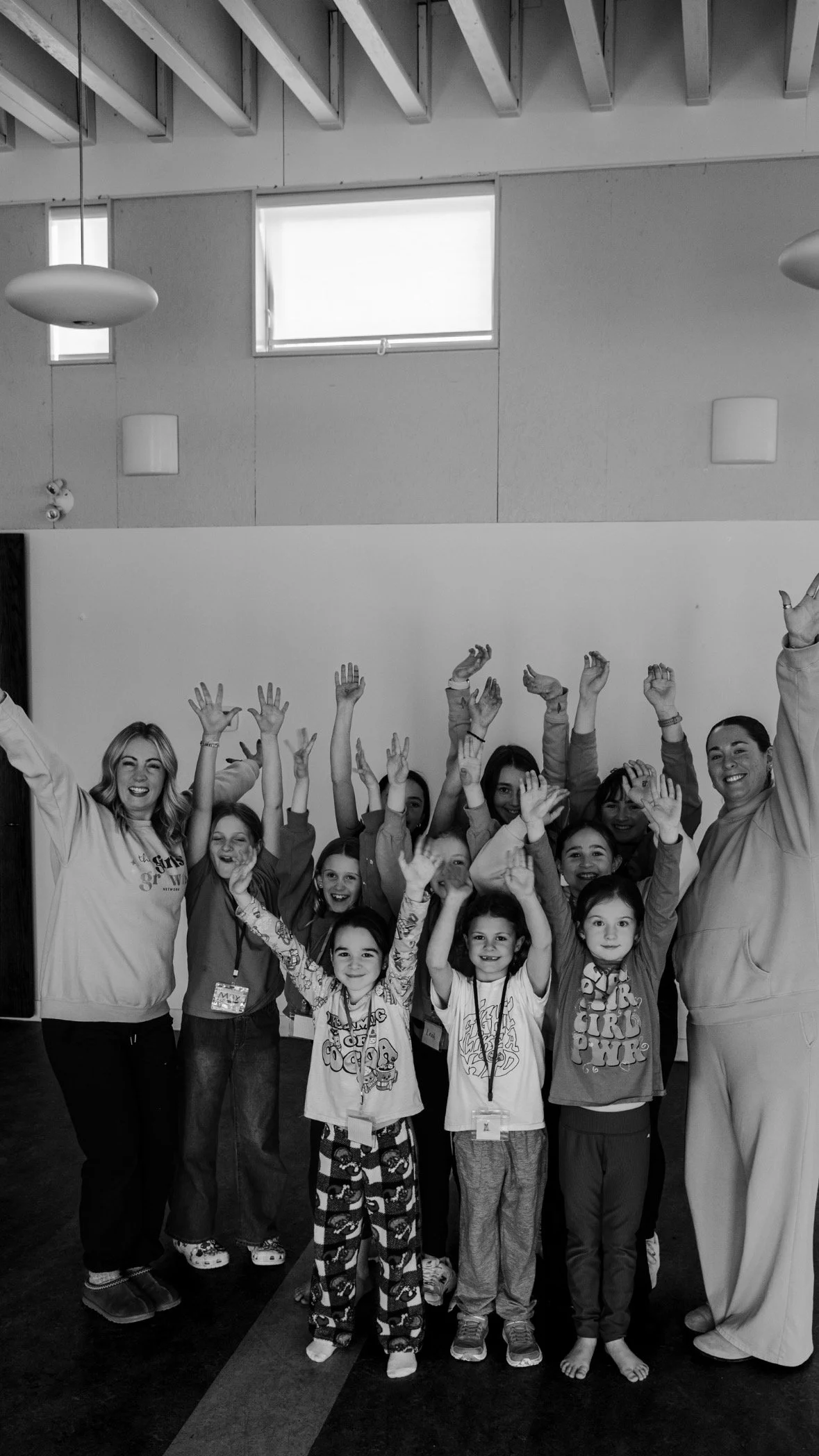Group of children and two adults indoors, smiling and raising their hands in celebration.