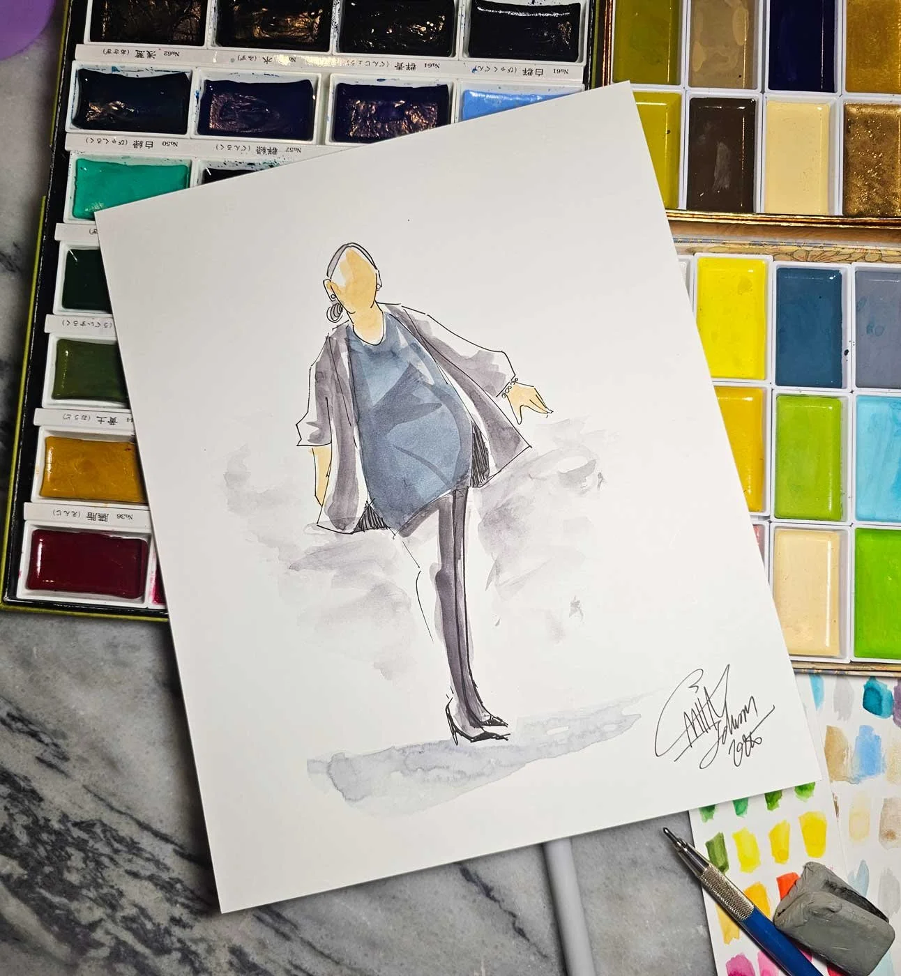 Close up of a painting of a woman in a black dress and cardigan laid on top of an assortment of watercolor pans.