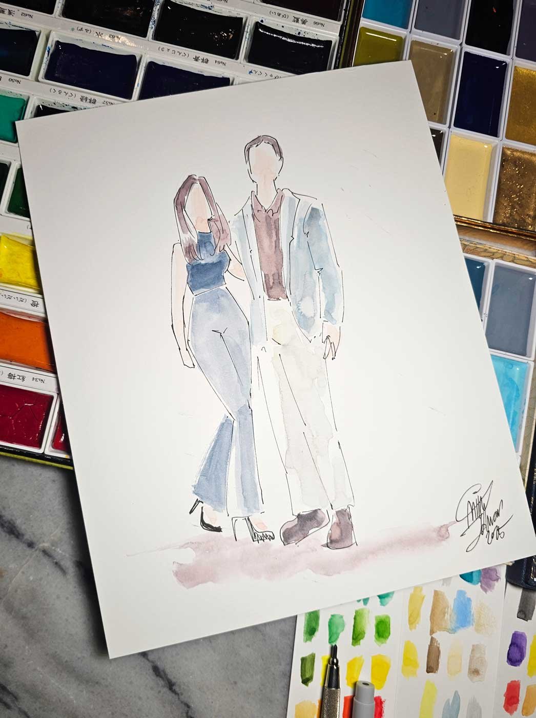 Close up of a painting of a woman and a man laid on top of an assortment of watercolor pans.