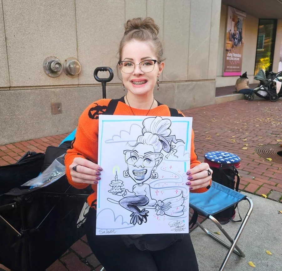 A woman with braces and an orange sweater holds up a caricature of her flying on a broom and holding a birthday cake.