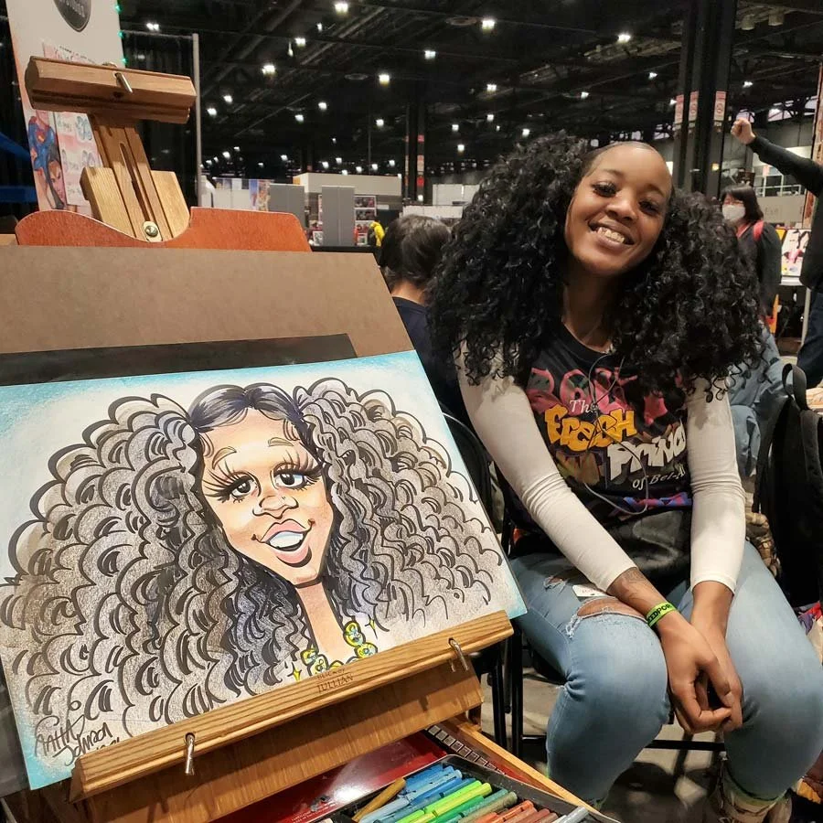 A woman with full curly hair is smiling while a caricature of her is on an easel.