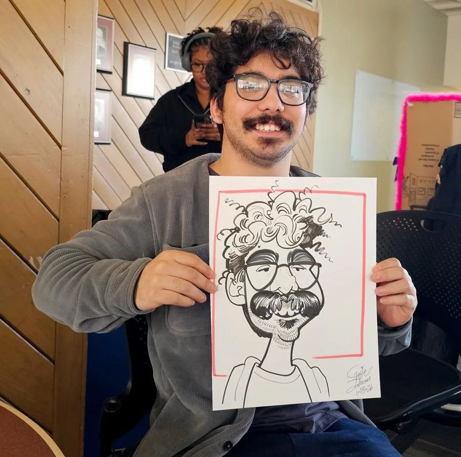 A man with glasses and a mustache is smiling and holding up his caricature.