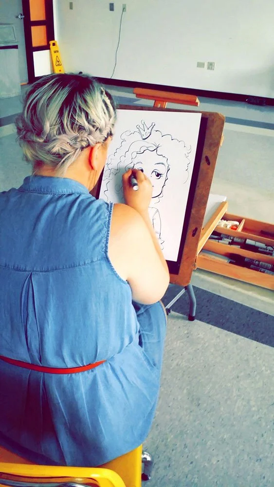 View of the artists back as she draws a little girl with a princess crown.
