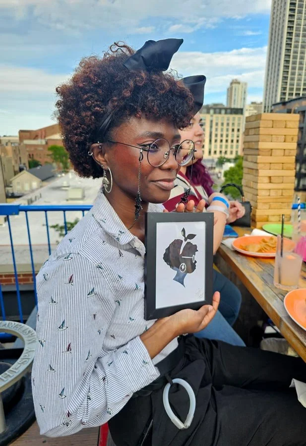 A woman with glasses and a bow holds up her framed silhouette.