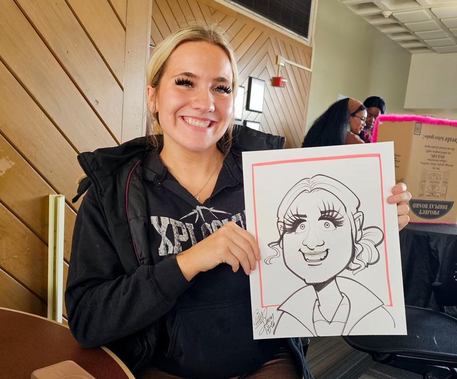 A blonde woman with long lashes is smiling while holding her caricature.