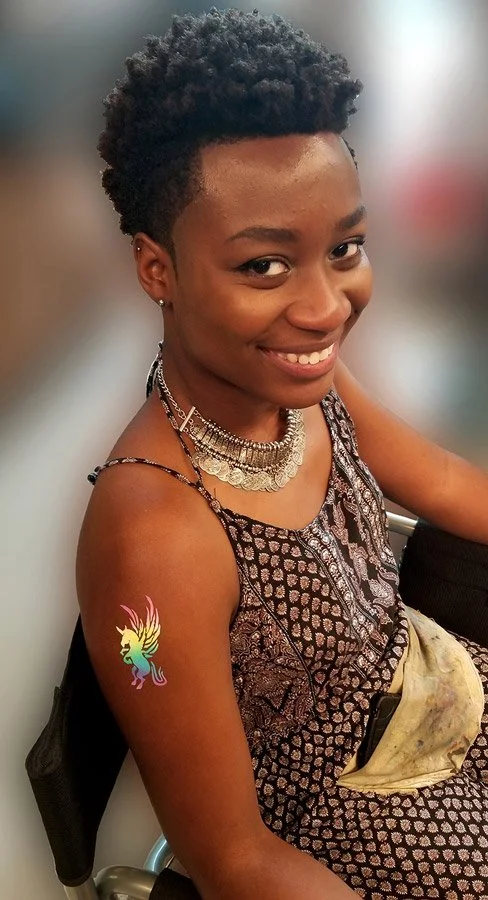 A smiling woman is showing off her rainbow pegasus temporary tattoo.
