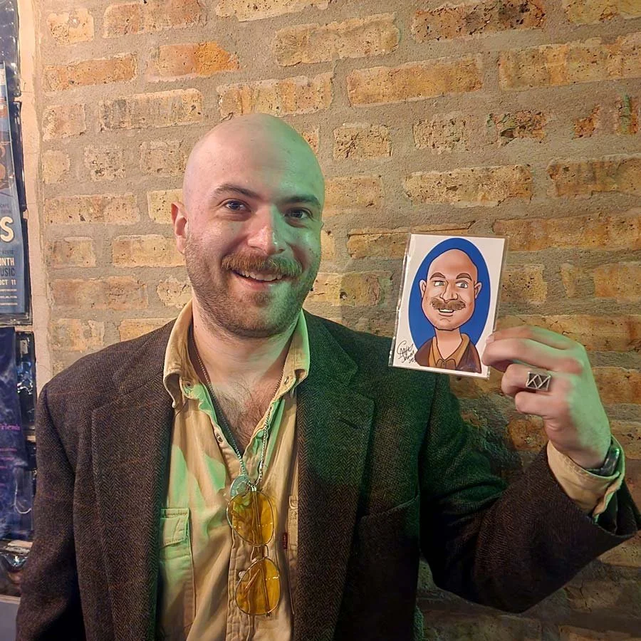 A man with a mustache and a suit jacket holds up his digital caricature print.