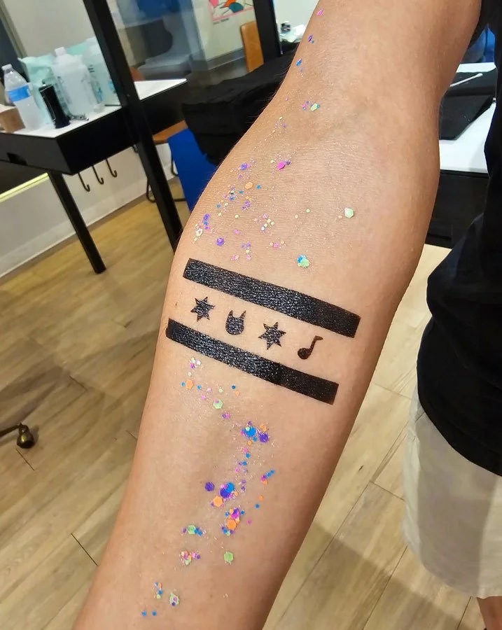 Temporary tattoo of Chicago flag with 2 stars, rock & roll hand symbol, and music note in black ink with glitter around the design.