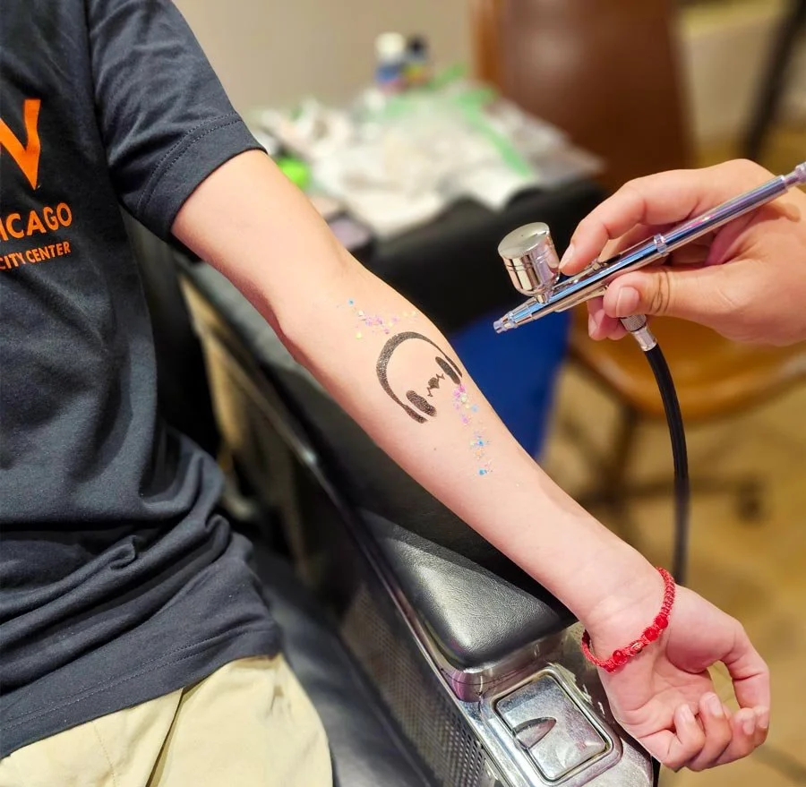 Artist airbrushing black headphone design on arm with glitter around it.