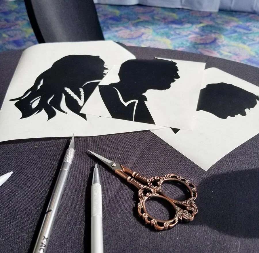 Three silhouettes are on a table next to scissors and craft knives.