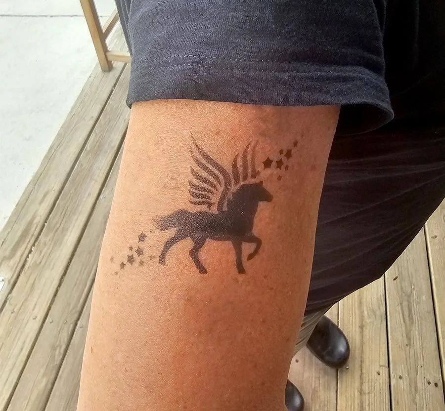 Close up of a black pegasus tattoo with star clusters around the design.
