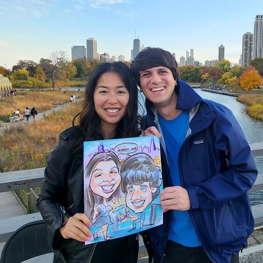 A smiling couple holds a caricature of the man proposing to the woman with the Chicago skyline in the background.