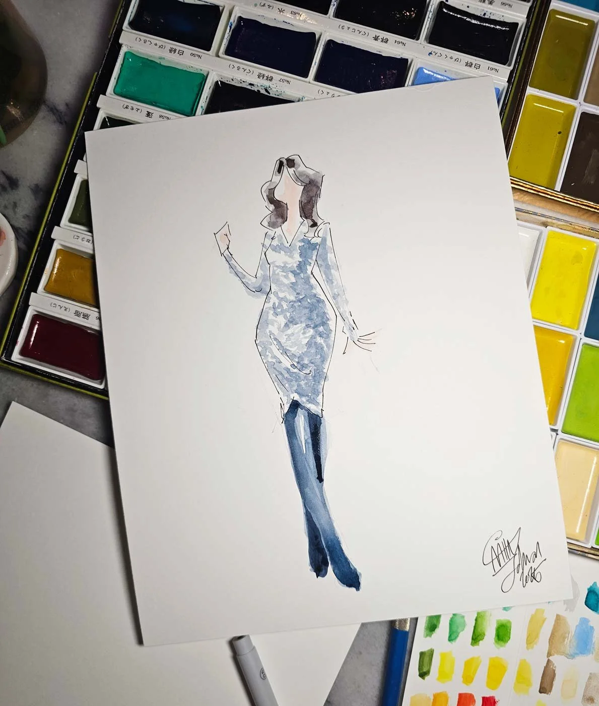 Close up of a painting of a woman in a sparkly gray dress and dark tights laid on top of an assortment of watercolor pans.