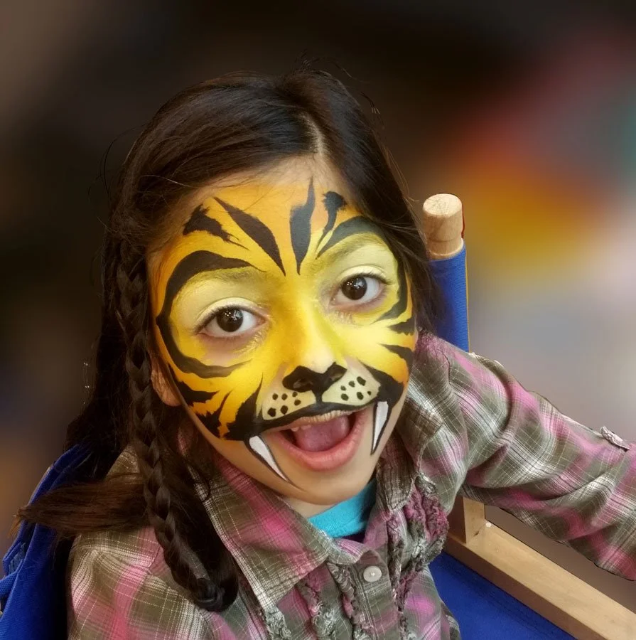 A girl makes a face while wearing a yellow tiger face paint.