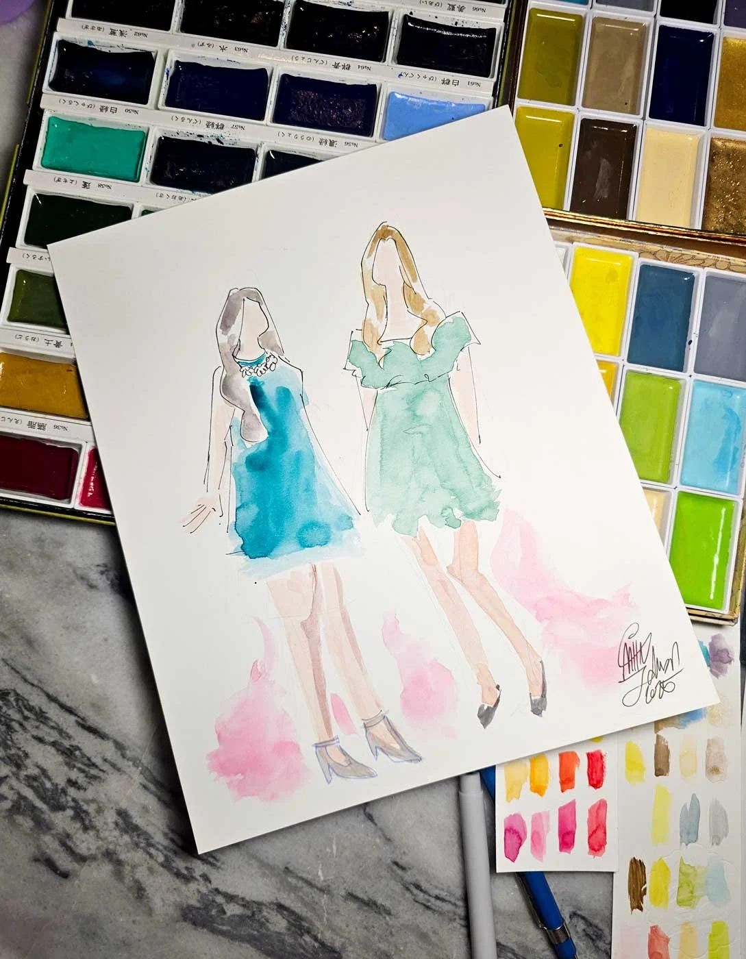 Close up of a painting of 2 women in green dresses laid on top of an assortment of watercolor pans.