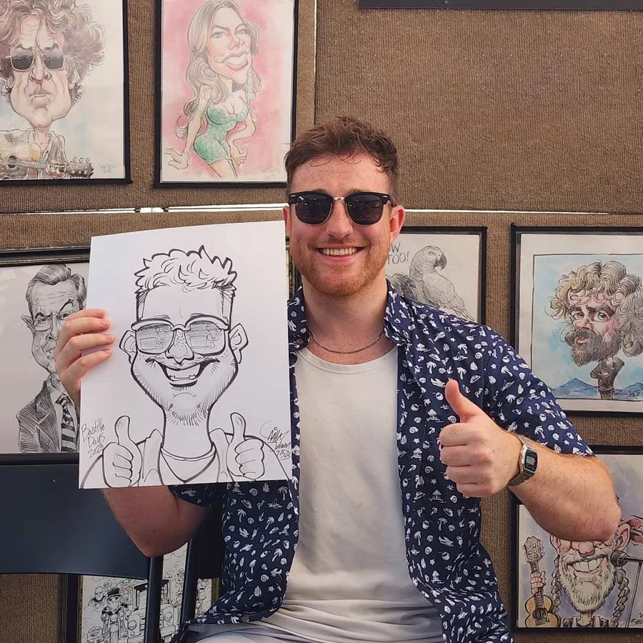 A man in sunglasses is giving a thumbs up while holding his caricature.