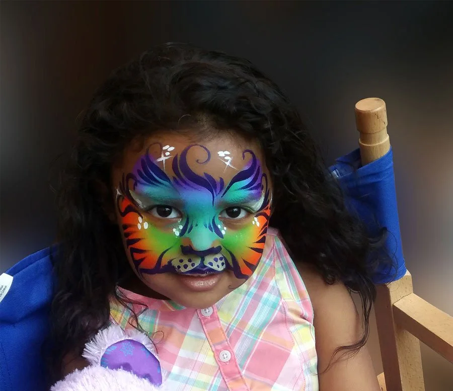 A girl is wearing a rainbow kitty face paint.