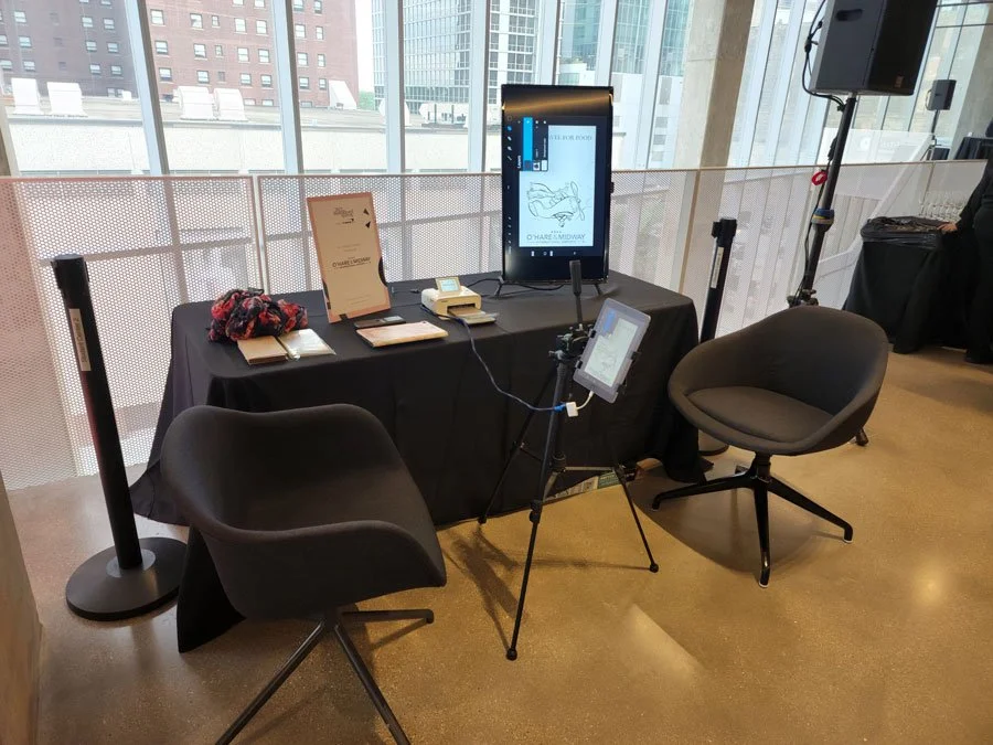 A digital display is on a table with 2 chairs and a tripod with an iPad.