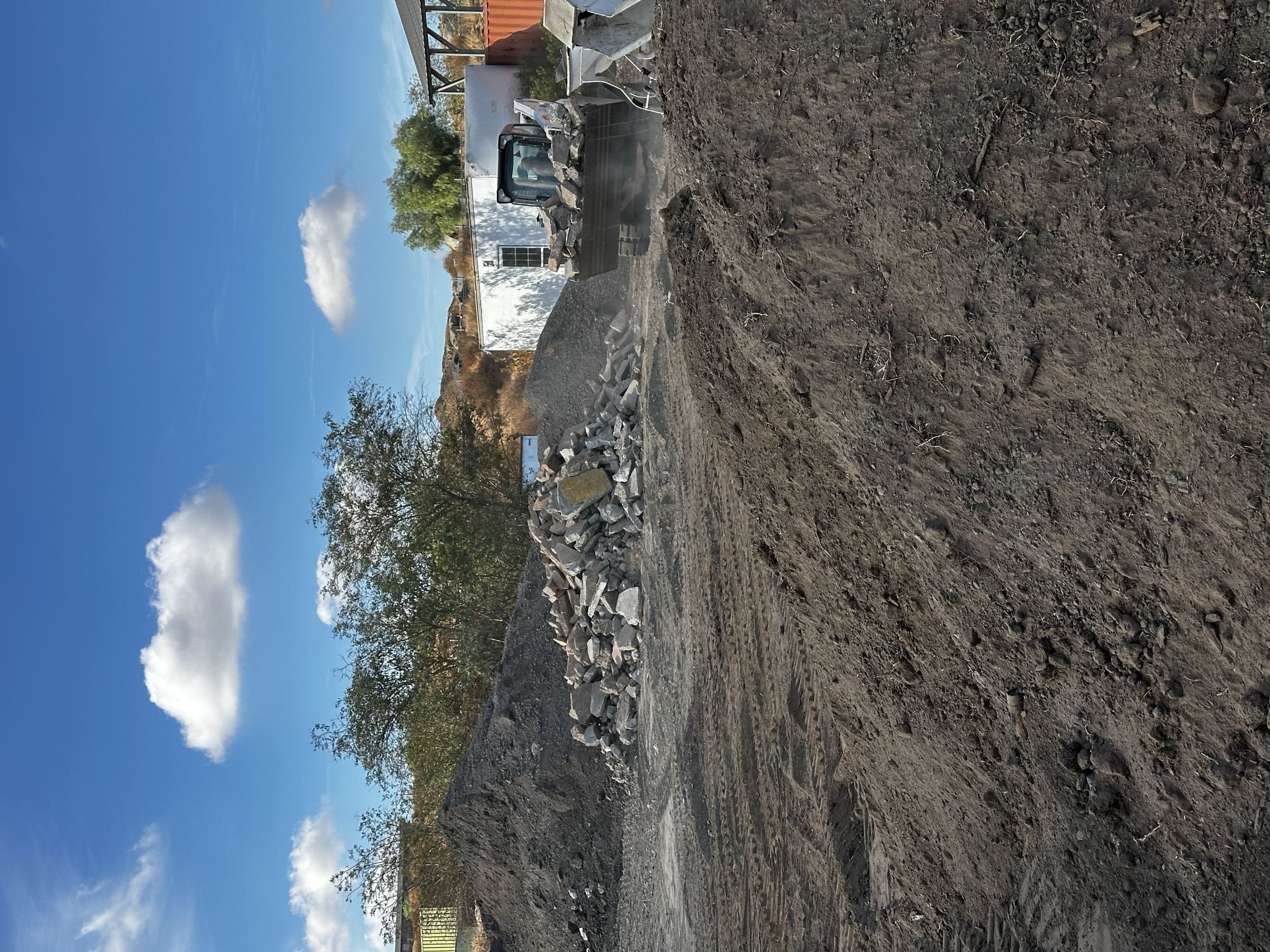 Construction site with a pile of rocks, a bulldozer, and dirt ground under a partly cloudy sky.