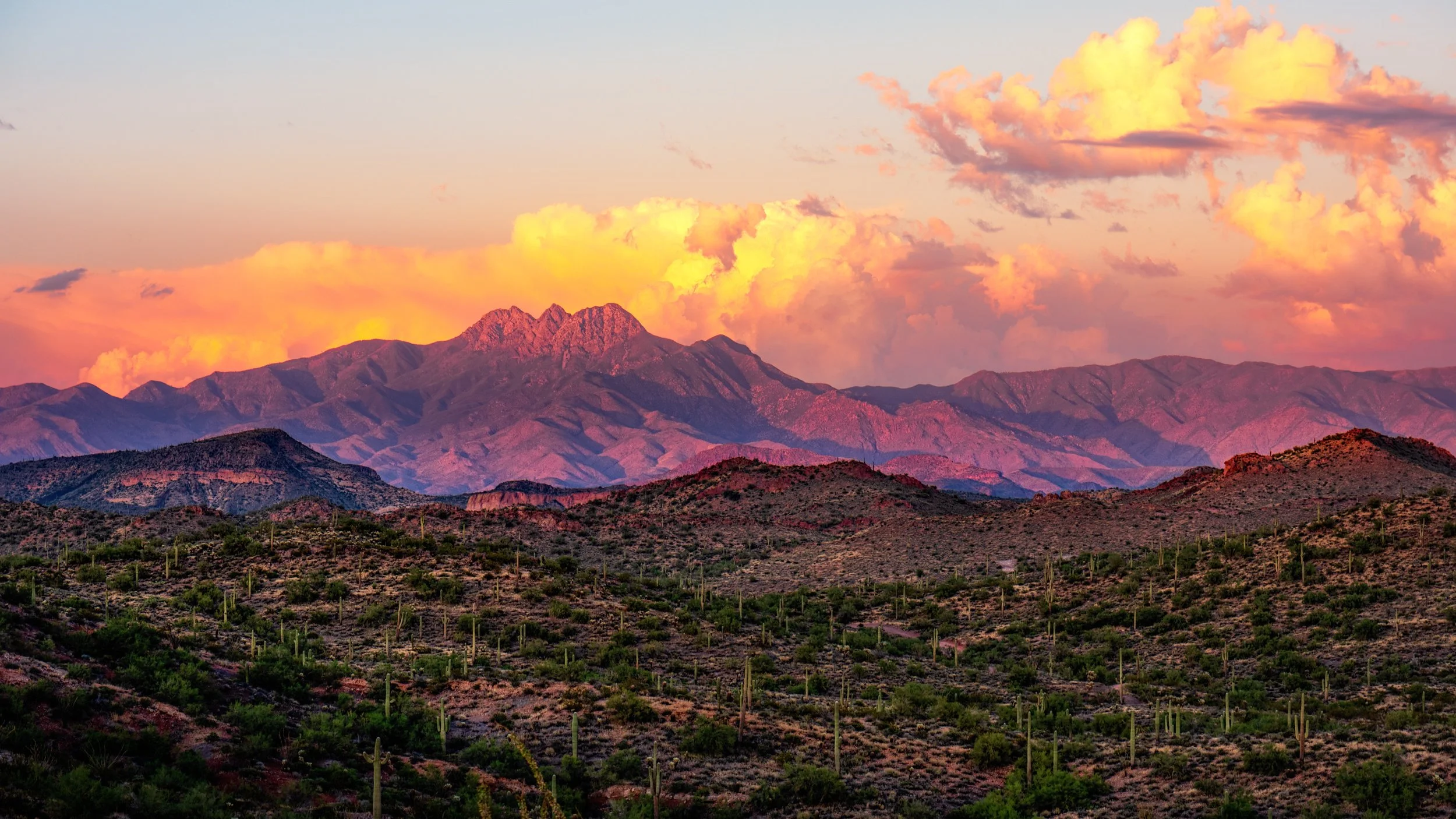Sunset over desert mountains in Arizona, with orange and purple clouds above saguaro covered hills