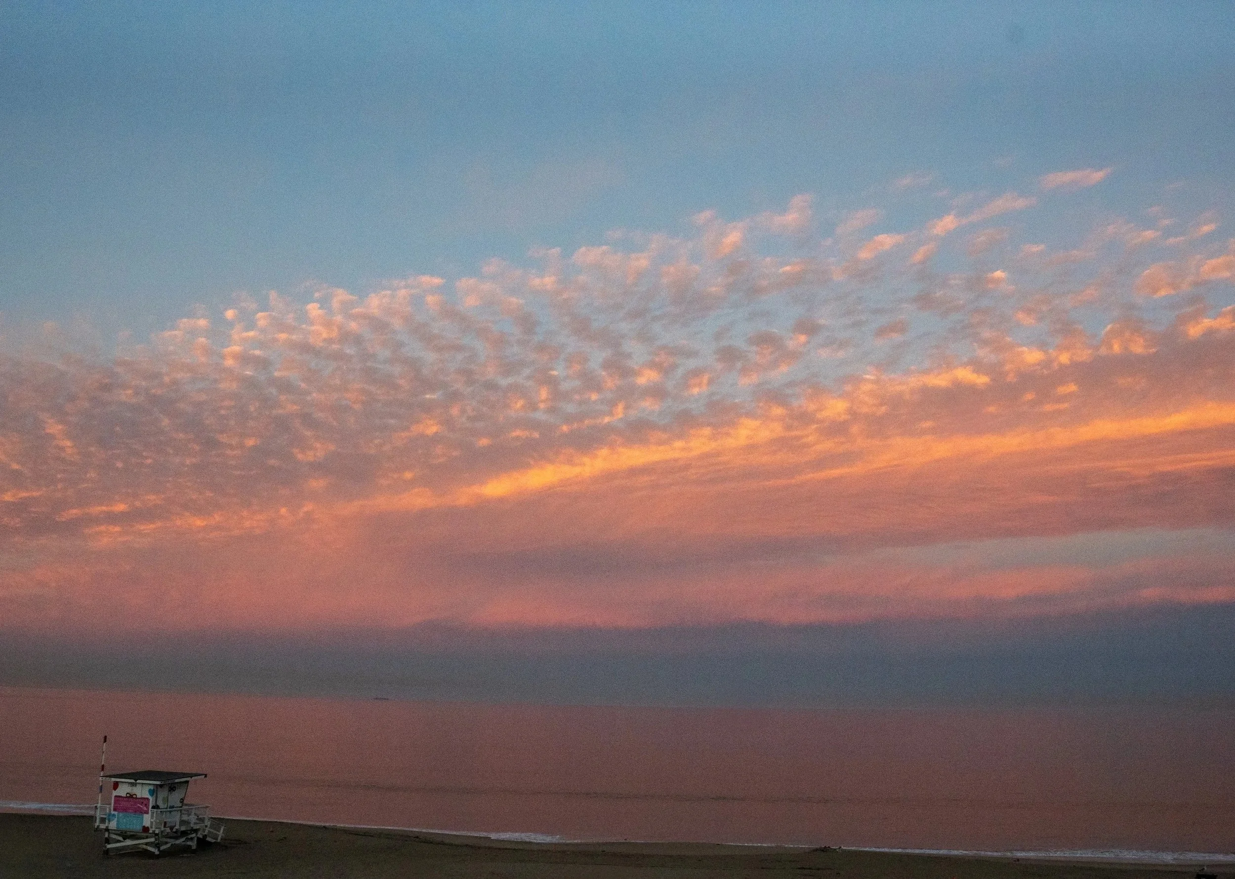 Pastel sunrise sky over the Pacific Ocean with a lifeguard tower on a quiet Southern California beach.