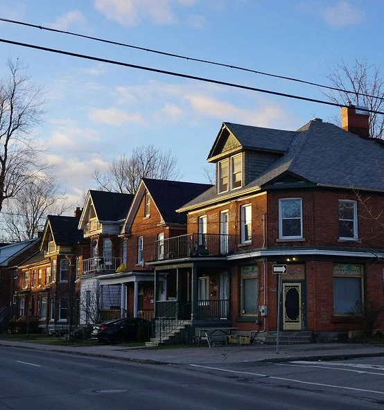 Row of brick houses with front porches on a residential street, under a partly cloudy sky.