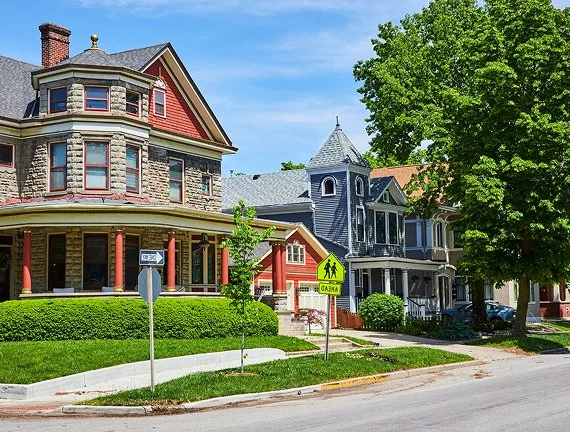 Houses on a tree-lined street with a pedestrian crossing sign in front.