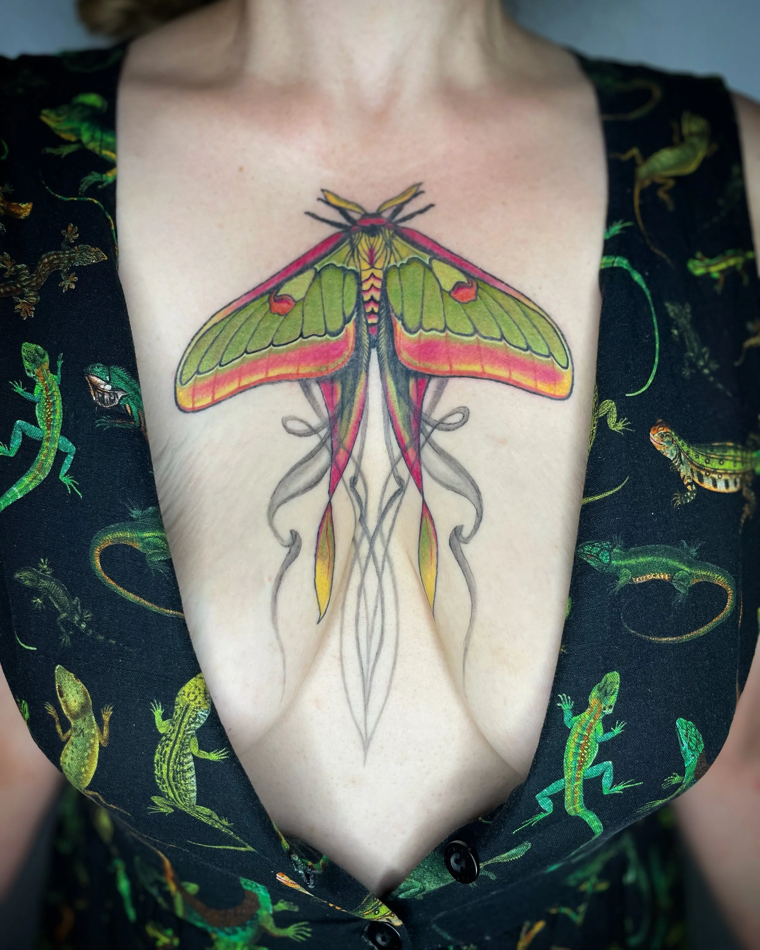 Colorful moth tattoo on person's chest, with a lingerie top featuring lizard patterns.