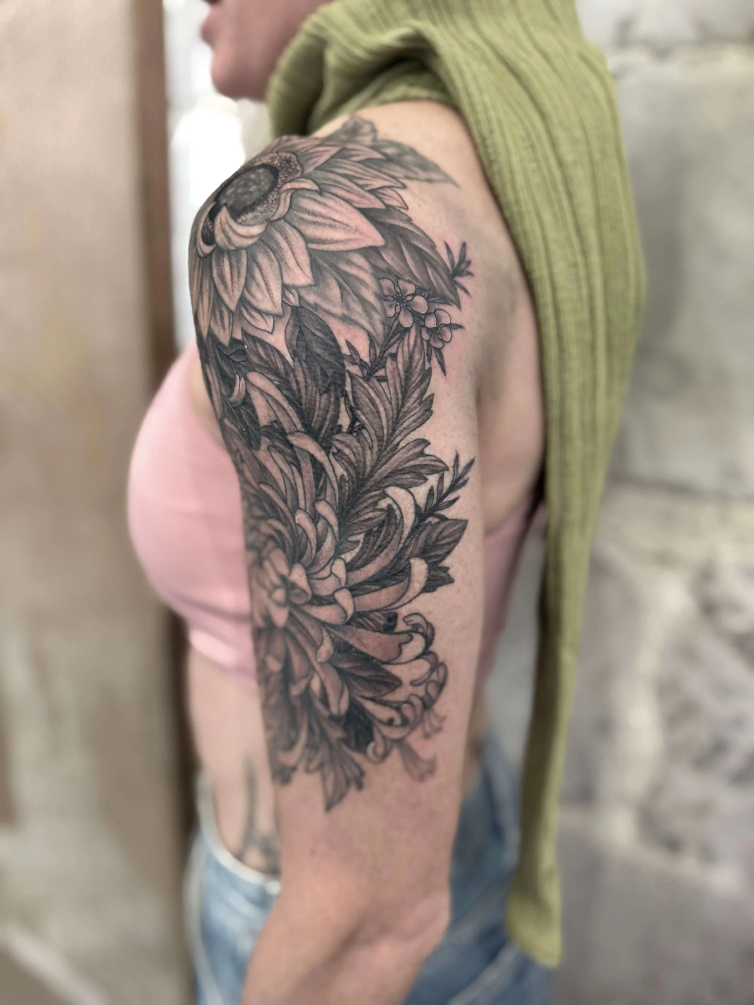 Close-up of a woman's upper arm with a detailed black and gray floral tattoo, showing large blossoms and leafy stems.