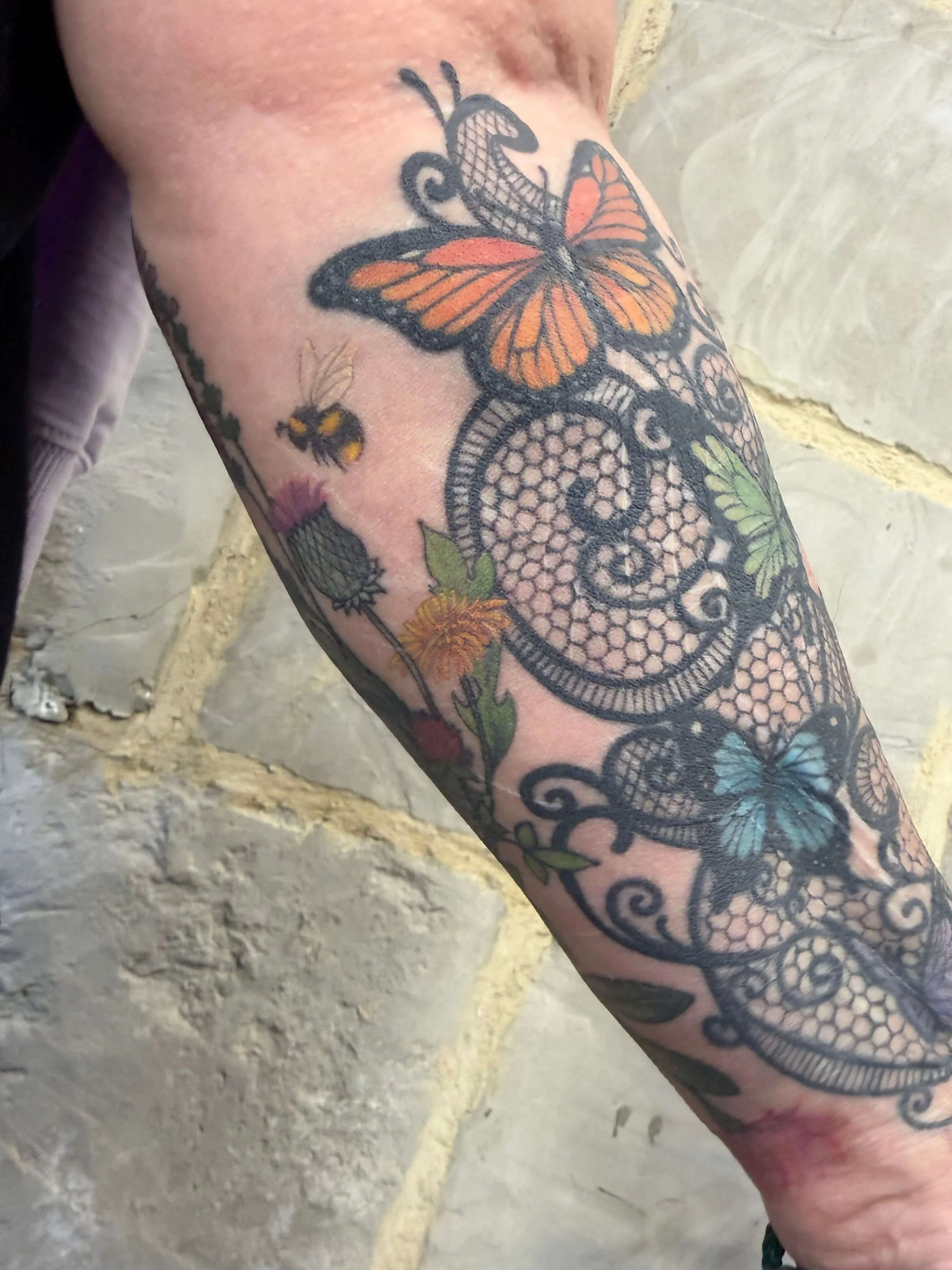Colorful tattoo sleeve featuring butterflies, bees, and floral elements on a person's forearm