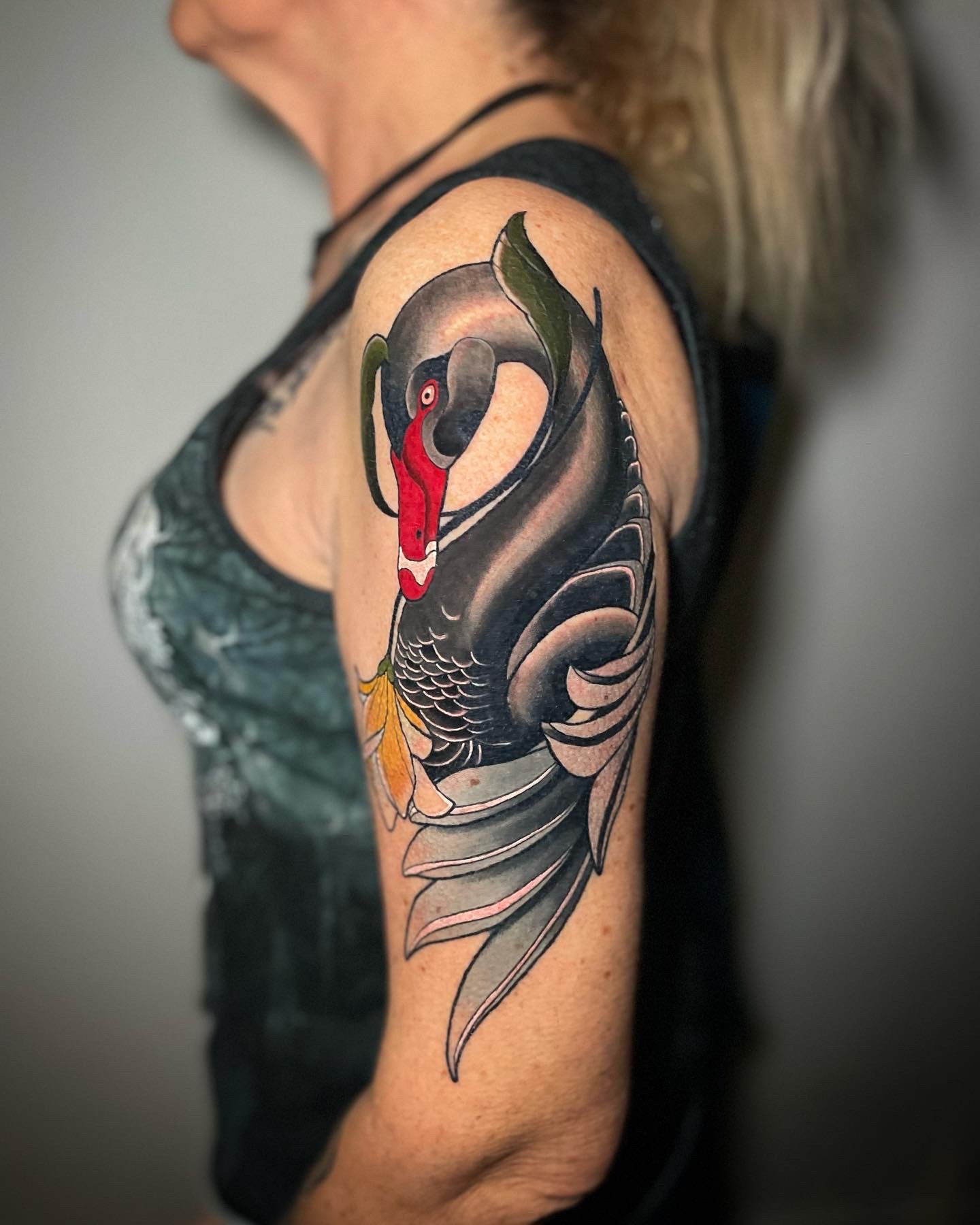 Tattoo of a black swan with a red beak on a person's upper arm.