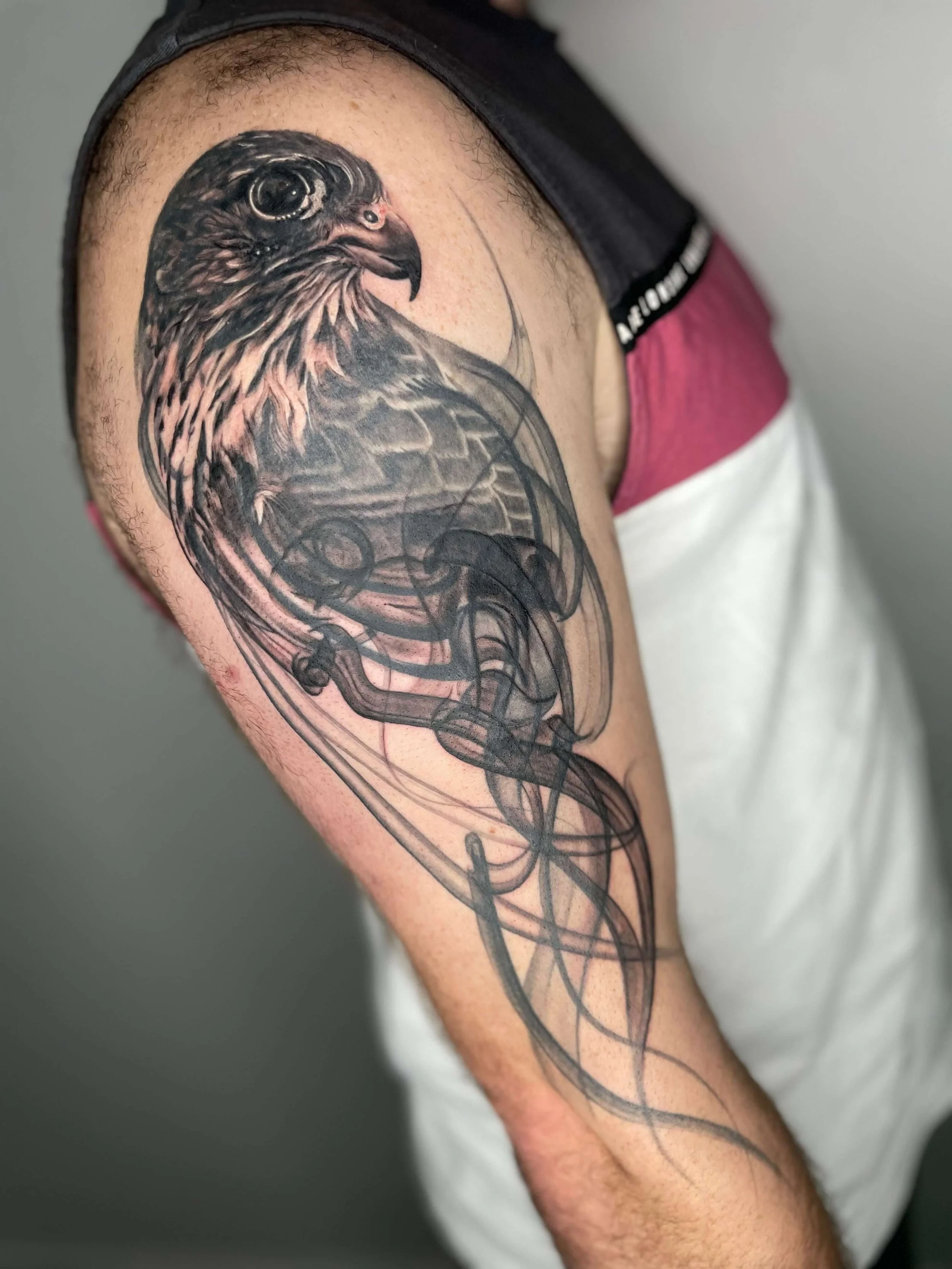 Tattoo of a hawk's head on a person's upper arm, with intricate linework and shading, including abstract patterns and design elements.