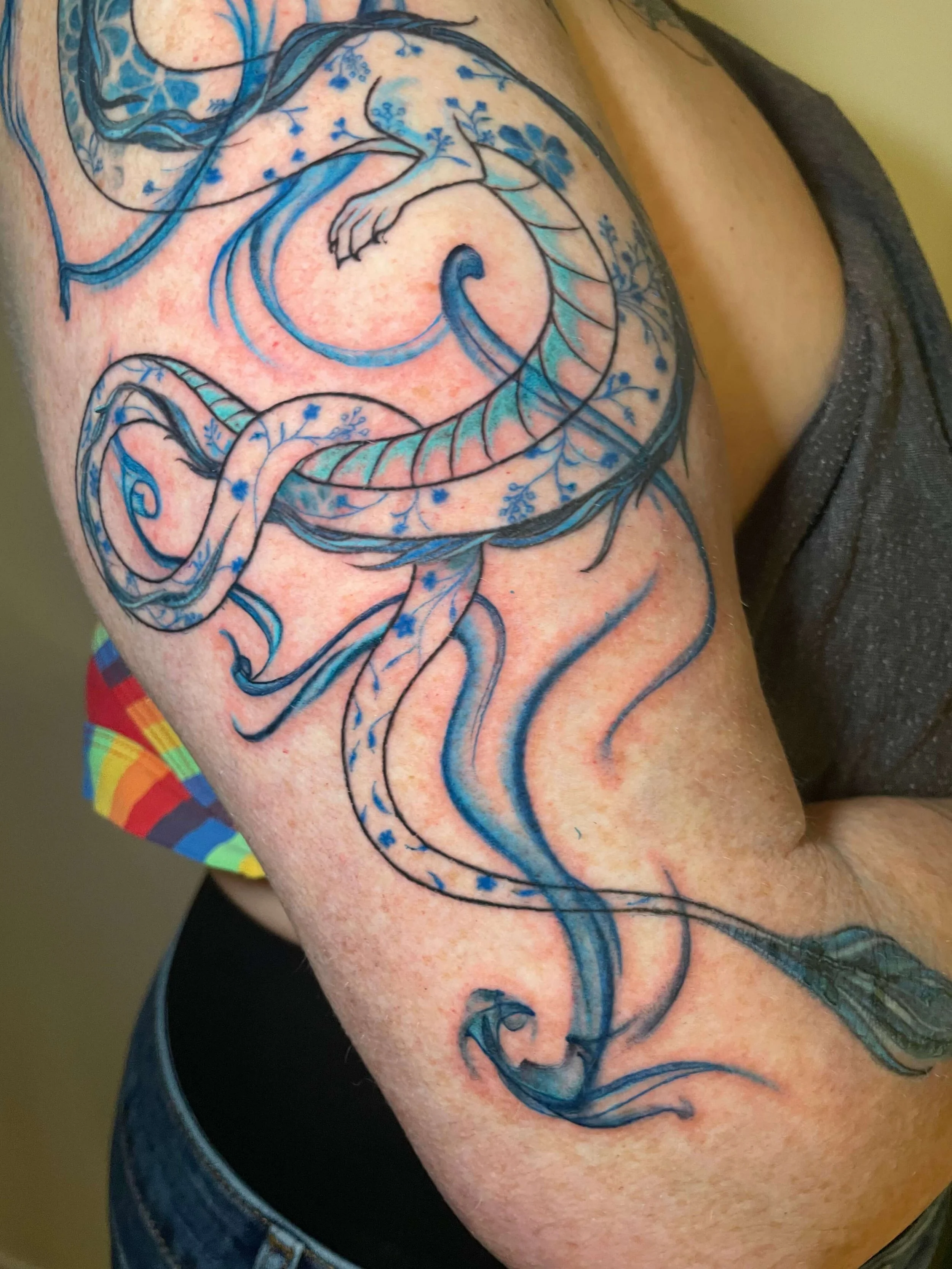 A tattoo of a blue and white dragon with floral details on a person's upper arm and shoulder.