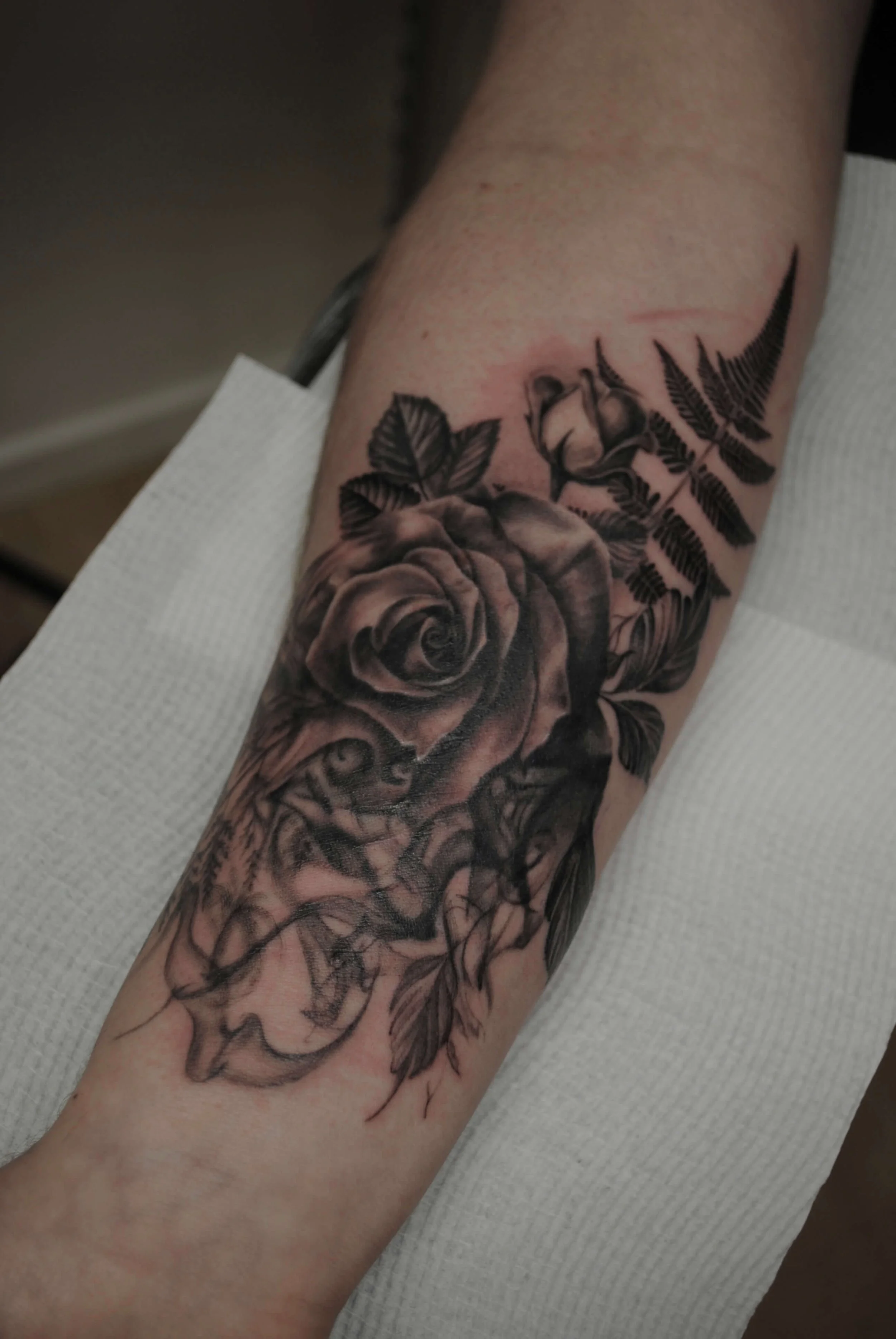 Black and gray tattoo of a detailed rose with leaves on a person's forearm.