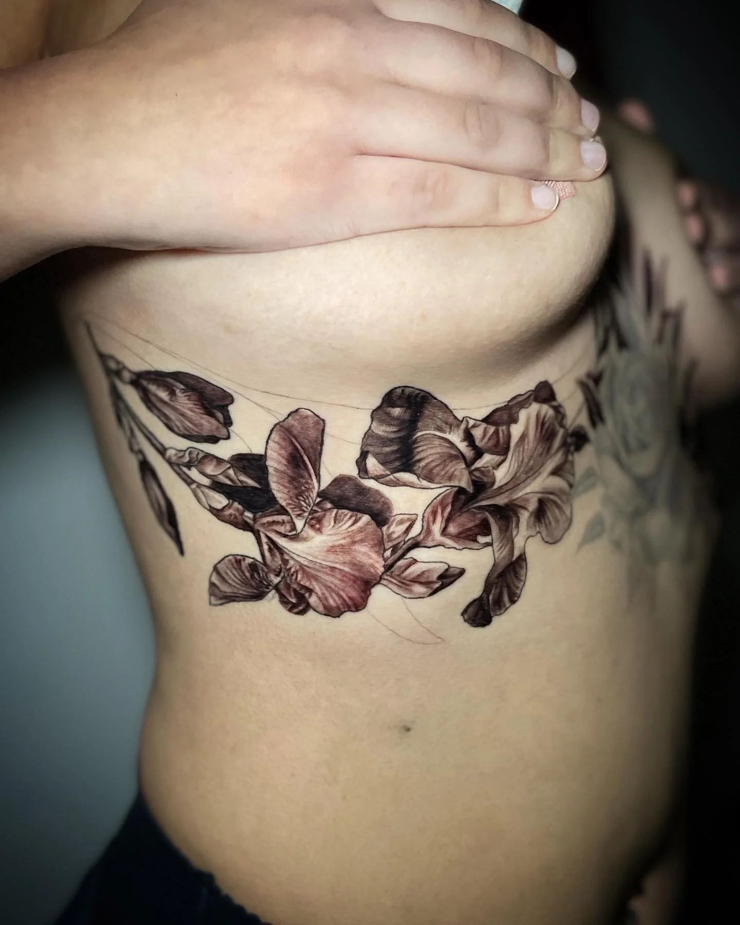 Close-up of a person's side torso with a floral tattoo in black and brown ink wrapping around the ribs.