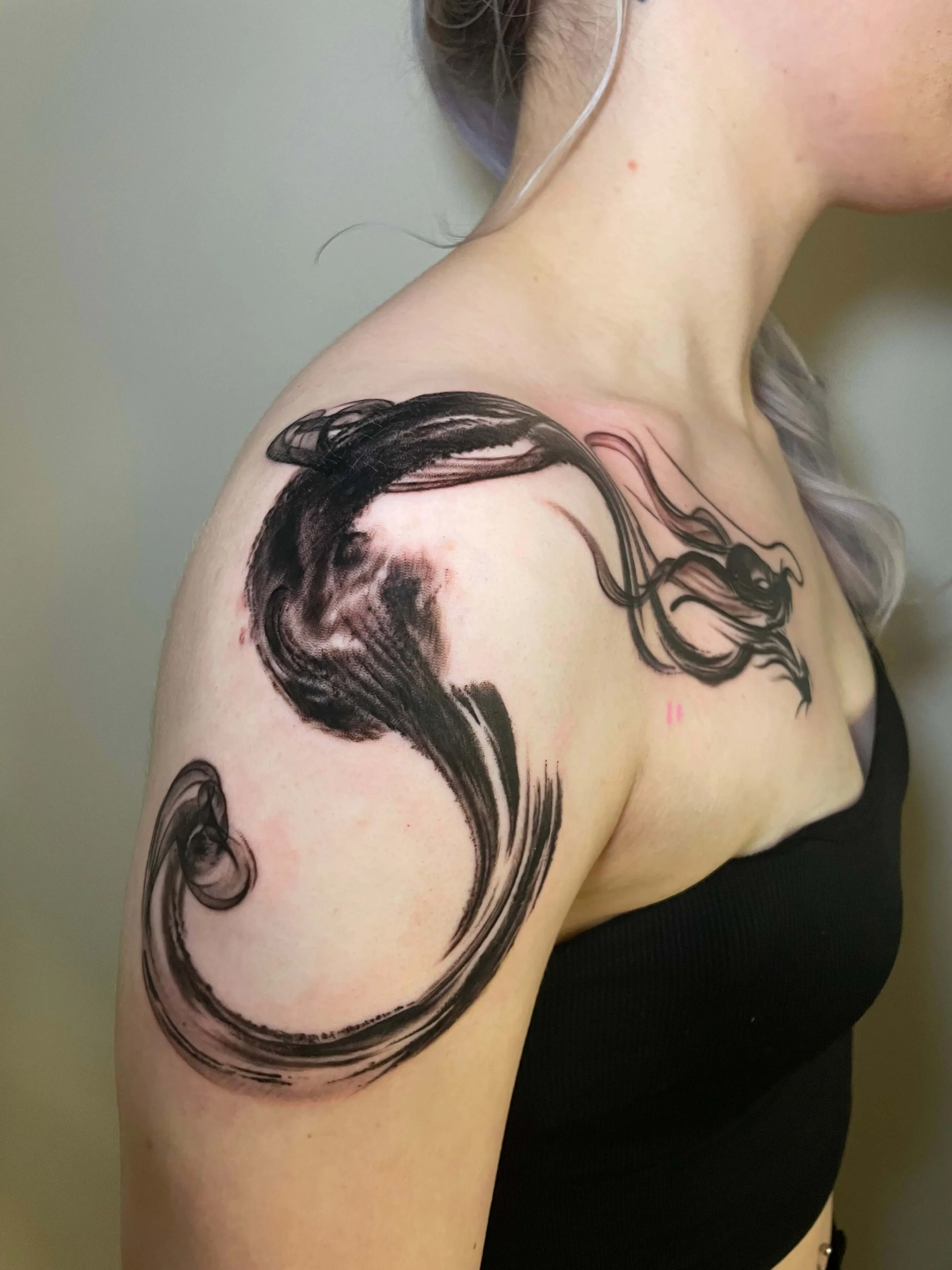 Tattoo of an abstract swirling black ink design on a person's shoulder and upper arm.
