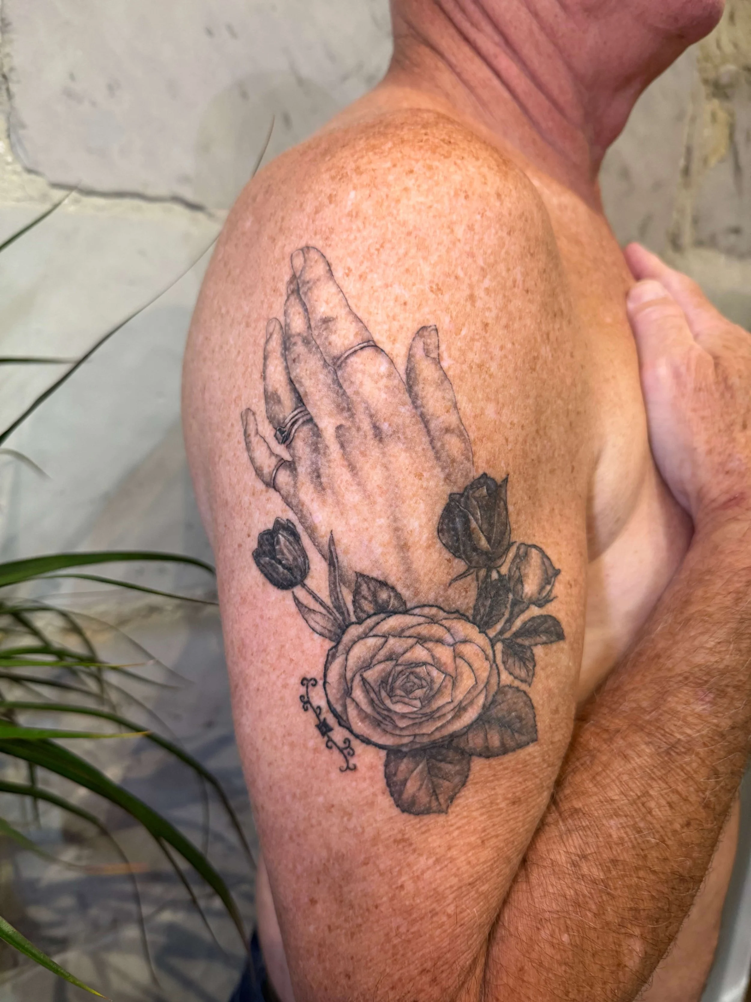 Tattoo of a hand with rings on the fingers, surrounded by roses and leaves, on a person's upper arm.