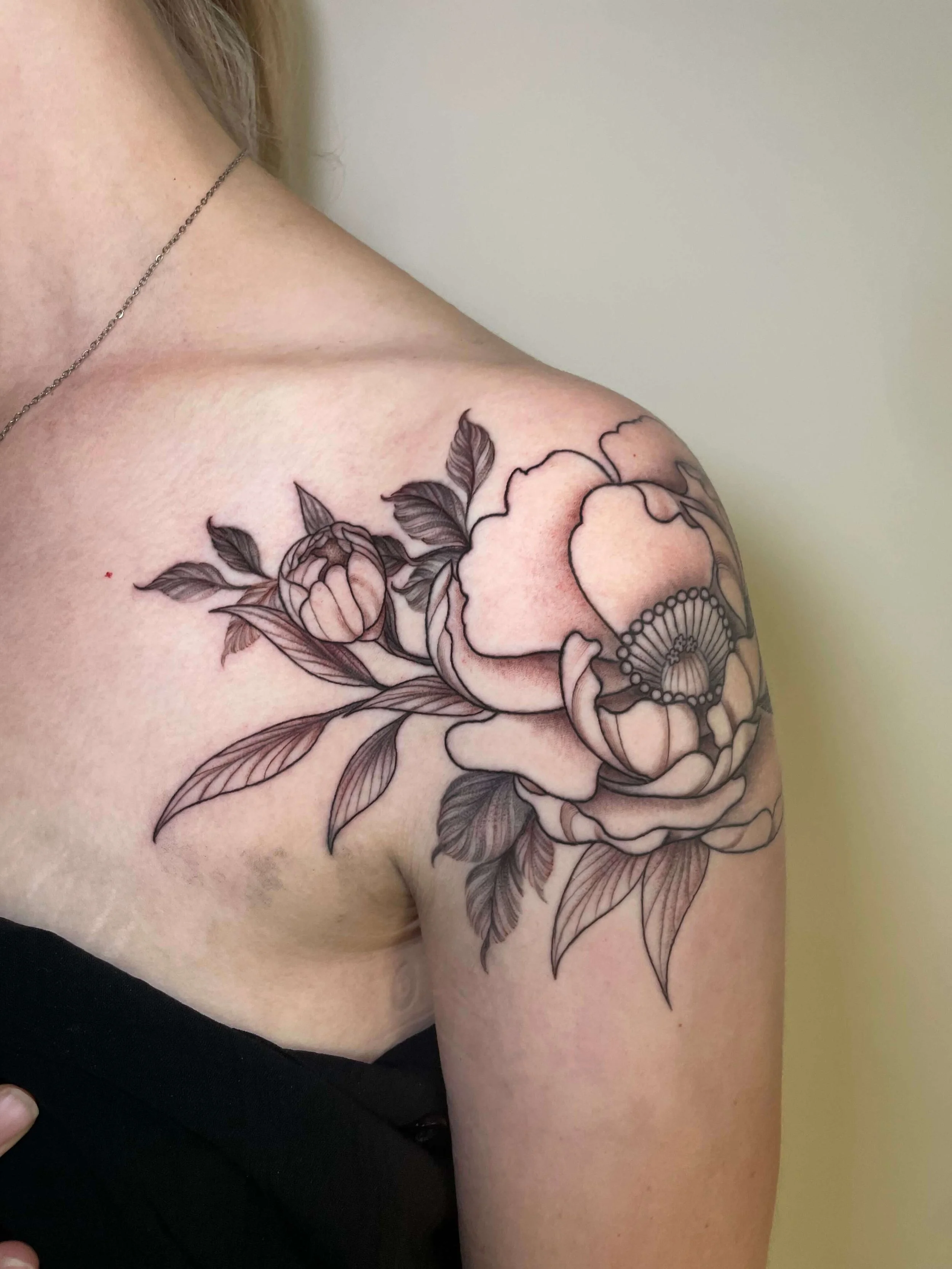 Black and gray floral tattoo of a rose and leaves on a person's shoulder